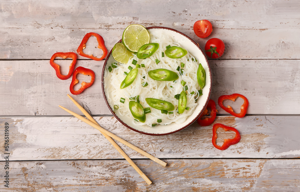 Bowl of tasty rice noodles with pepper, lime and chopsticks on light wooden background