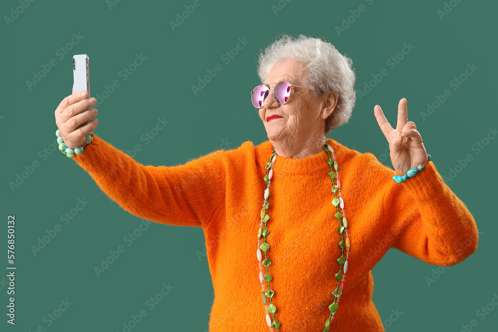 Senior woman with bright accessories taking selfie on green background