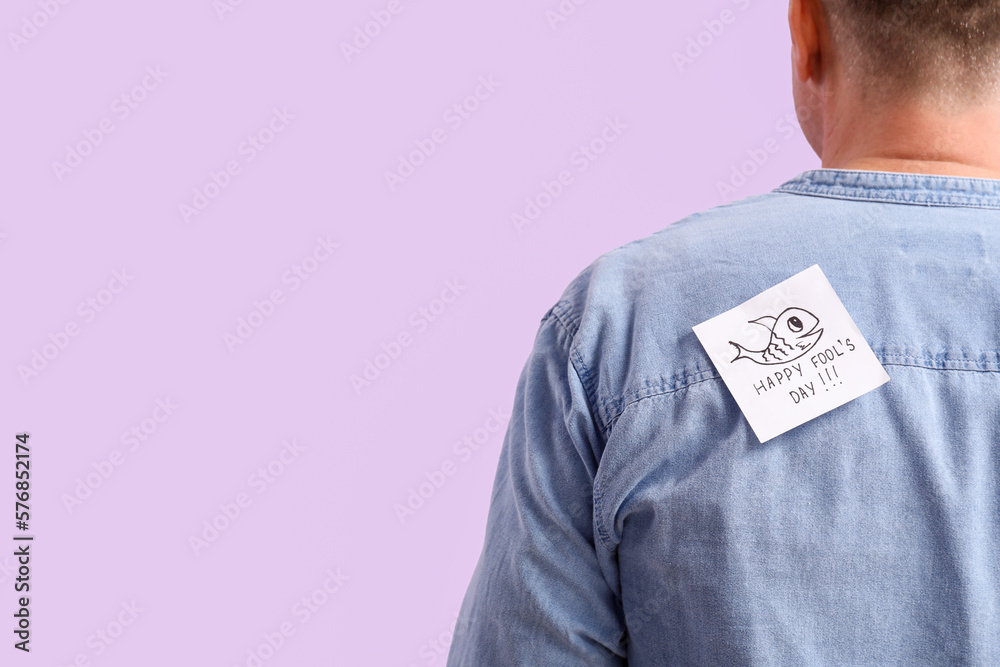 Sticky paper with text HAPPY FOOLS DAY on back of mature man against lilac background, closeup