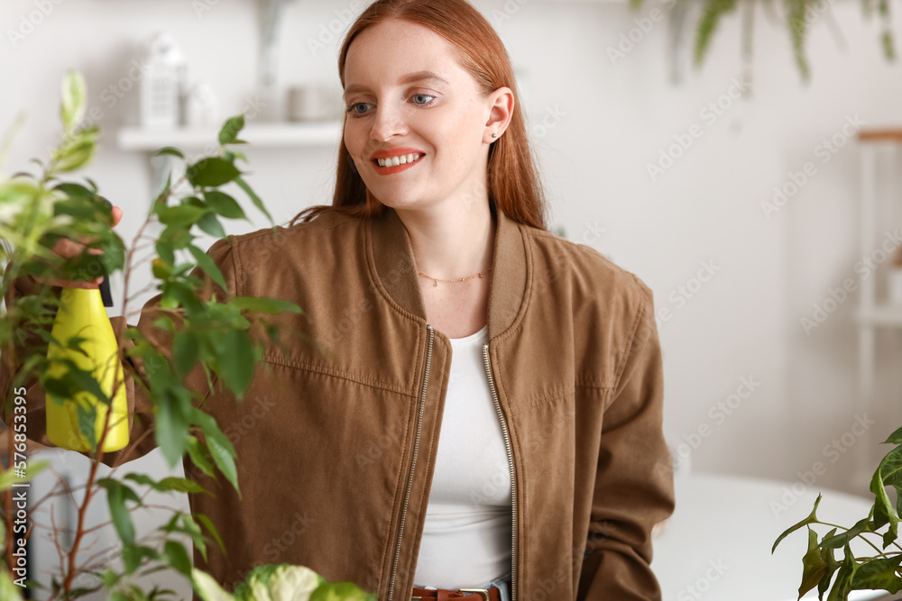 Young woman spraying water onto green houseplant at home