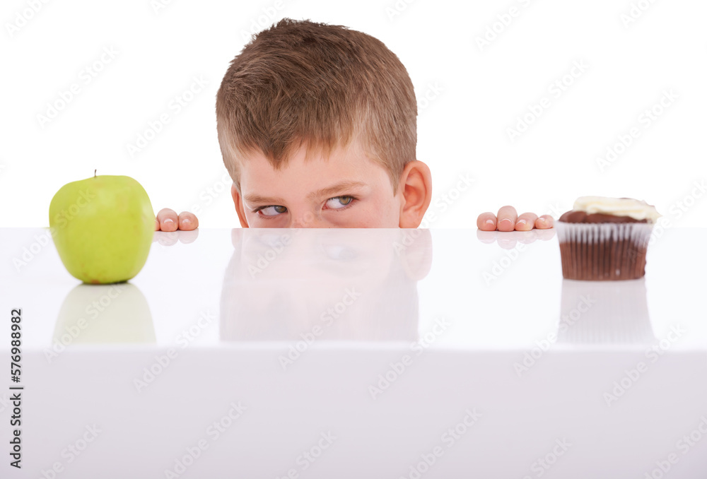 A young boy tempted by the sight of a chocolate cake and an apple on a table making an unhealthy dec