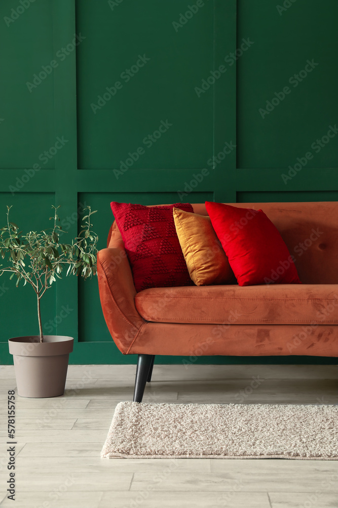 Red sofa with stylish cushions and houseplant near green wall