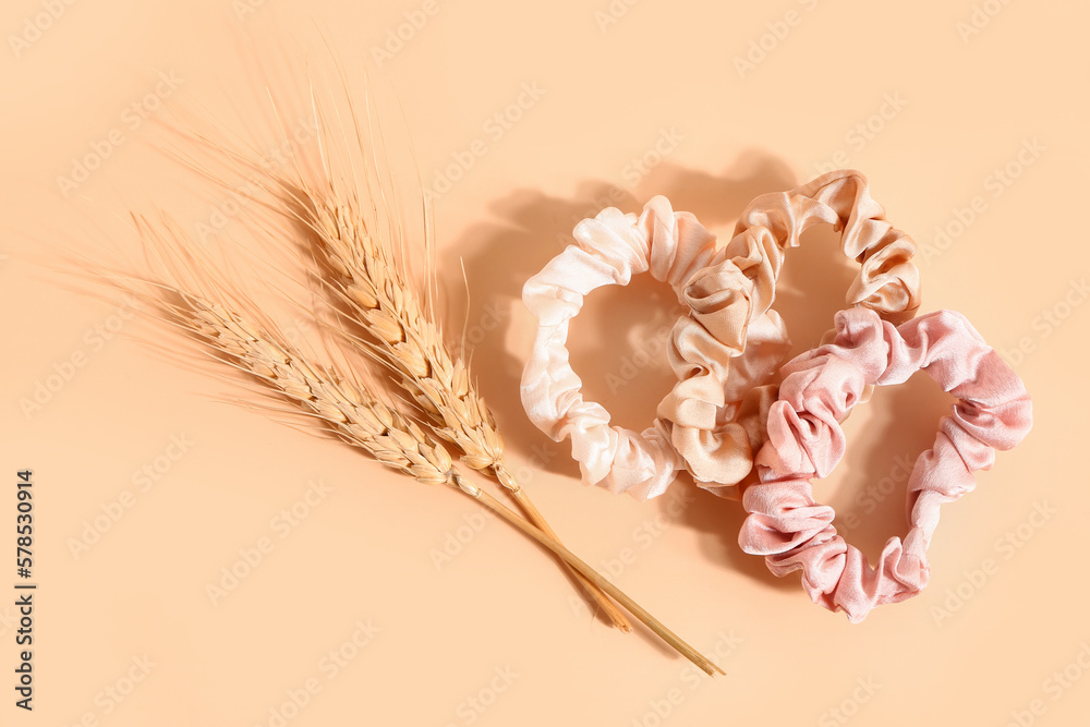 Silk scrunchies and wheat spikelets on color background