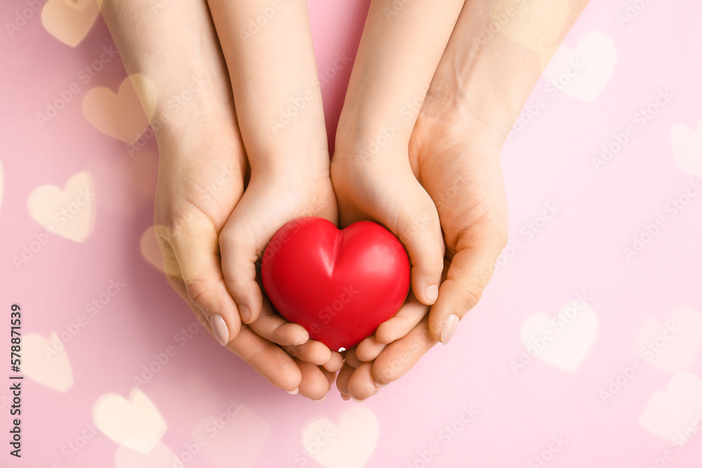 Hands of woman and child with red heart on pink background. Mothers Day