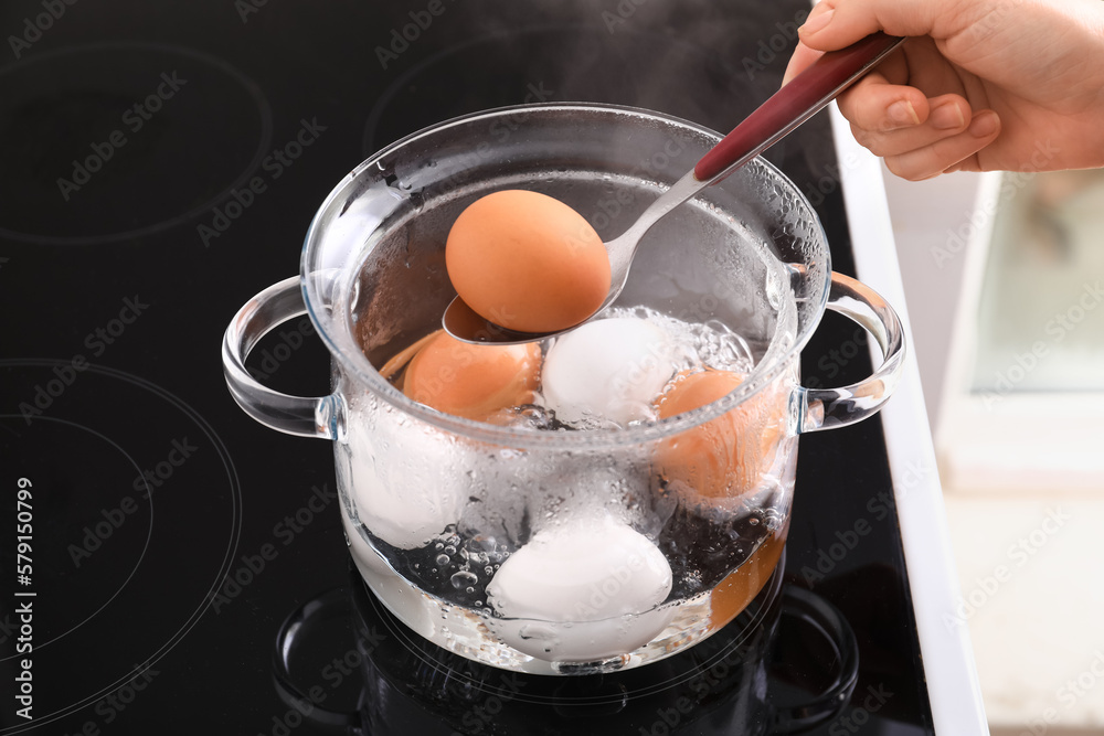 Woman holding spoon with boiled egg above cooking pot on stove, closeup