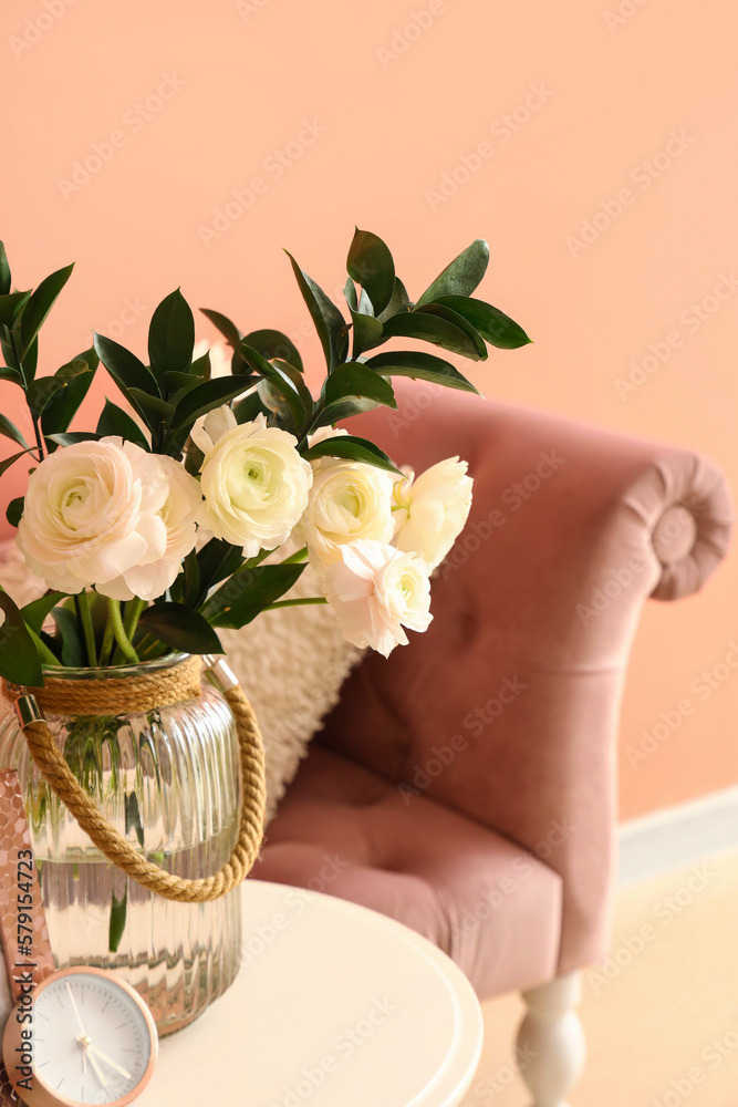 Vase with ranunculus flowers and clock on table in living room, closeup