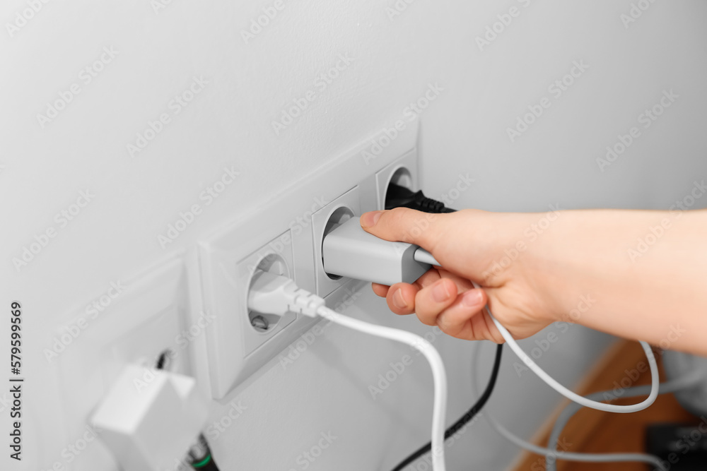 Woman putting plug into socket at home, closeup