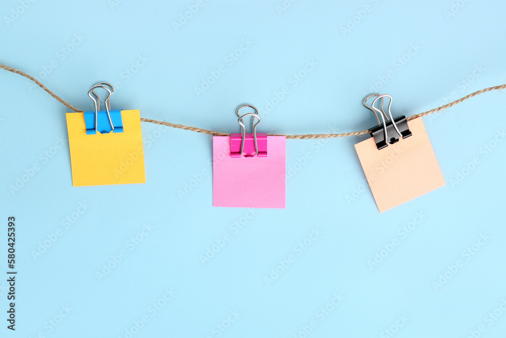 Sticky notes with binder clips hanging on rope against color background