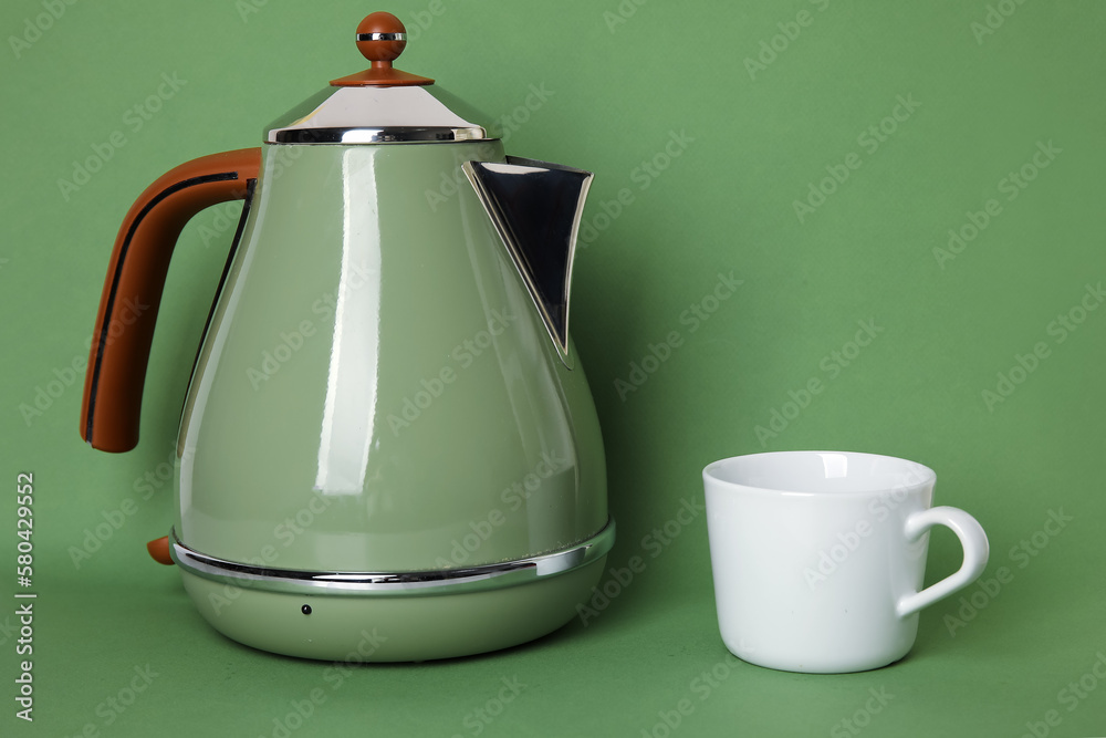 Electric kettle and cup on green background