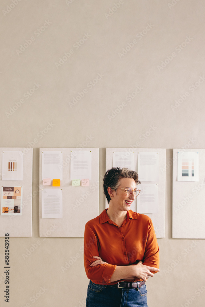 Mature designer looking away with a happy smile in her office