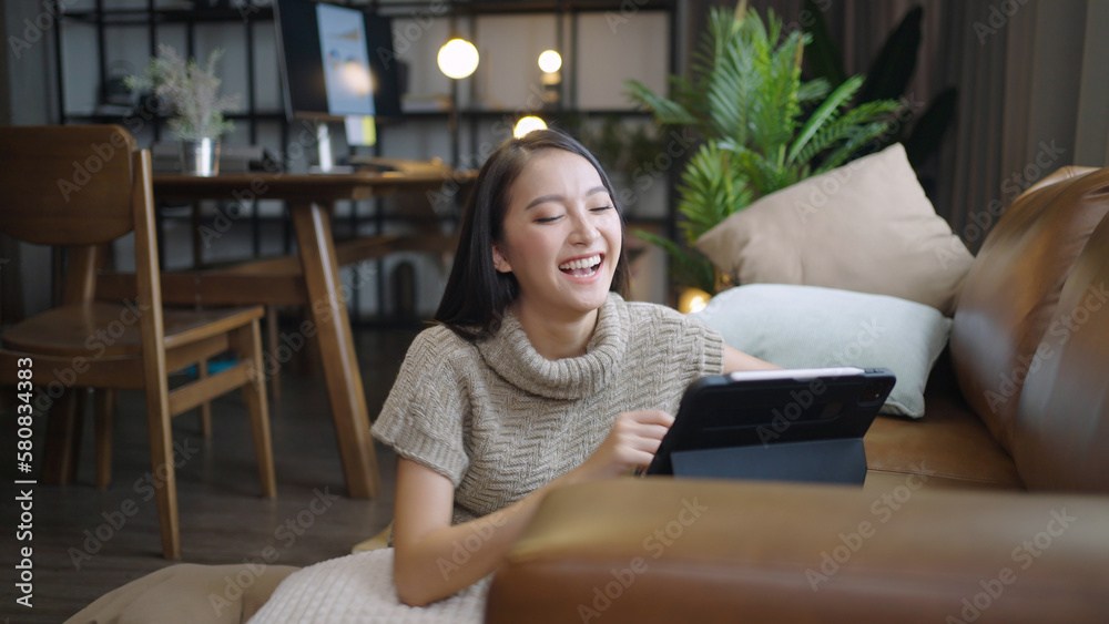 Asian woman happily using tablet to watch comedy series at home