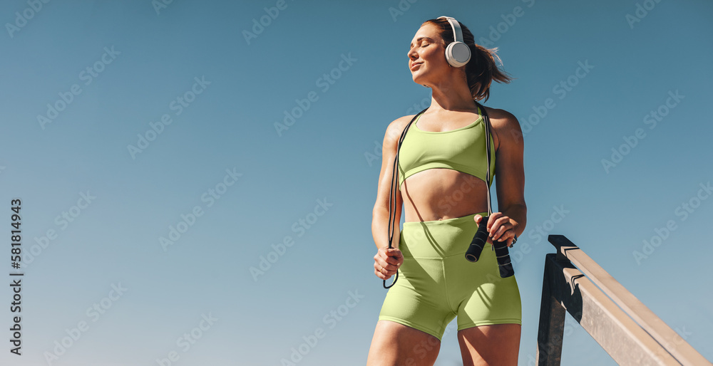 Female athlete in her 30s outdoors taking a break from her cardio workout, holding a skipping rope a