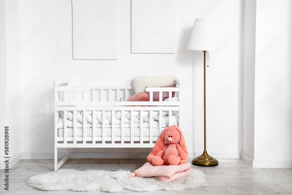 Interior of light childrens bedroom with baby crib, lamp and toy