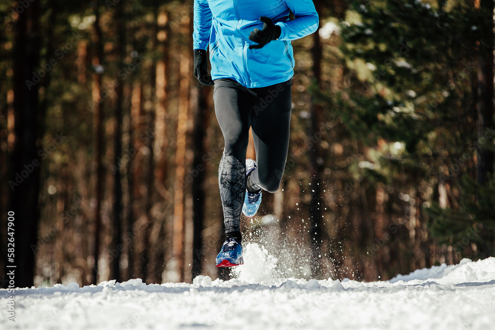 legs male runner running winter forest trail, splashes of snow underfoot, sports photo