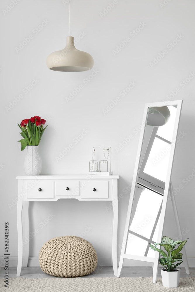 Interior of light room with mirror and tulips in vase on table