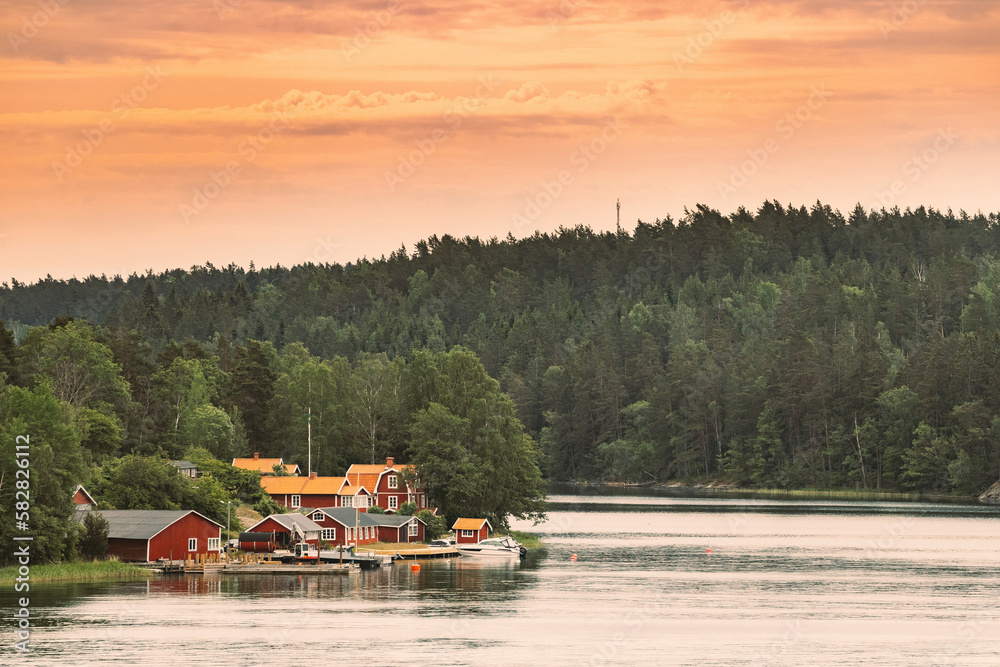 Sweden. Many Beautiful Red Swedish Wooden Log Cabins Houses On Rocky Island Coast. Lake Or River Lan