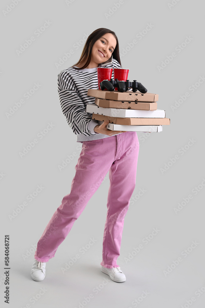 Young woman with boxes of tasty pizza, game pads and cups on grey background