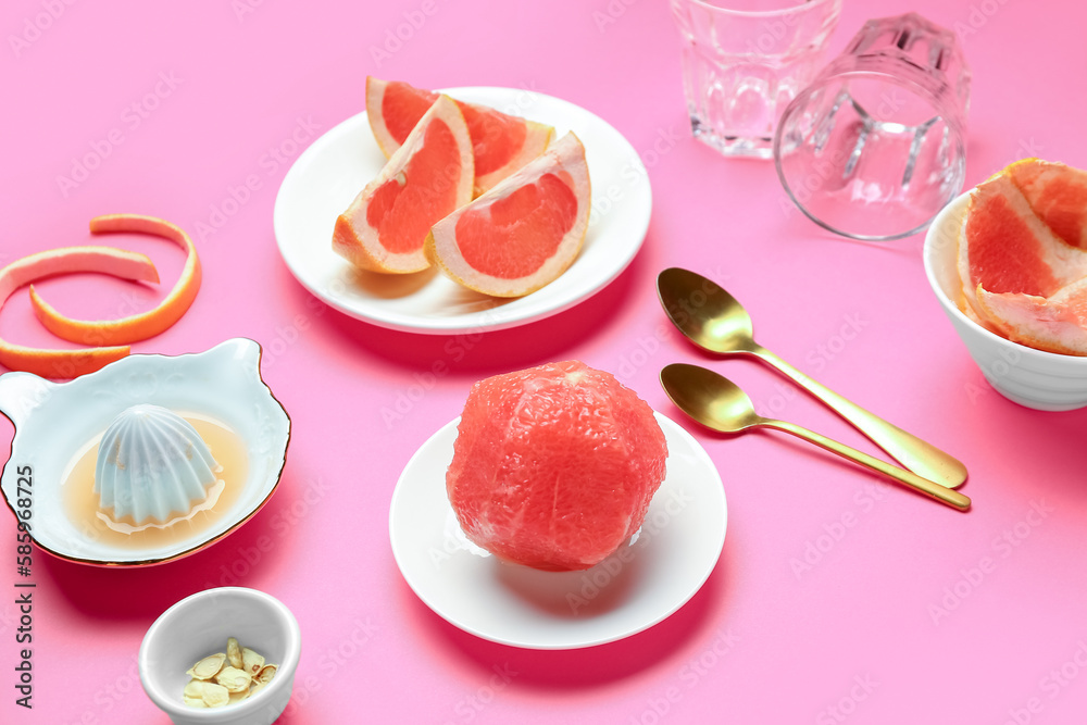 Plates with ripe grapefruits and juicer on pink background