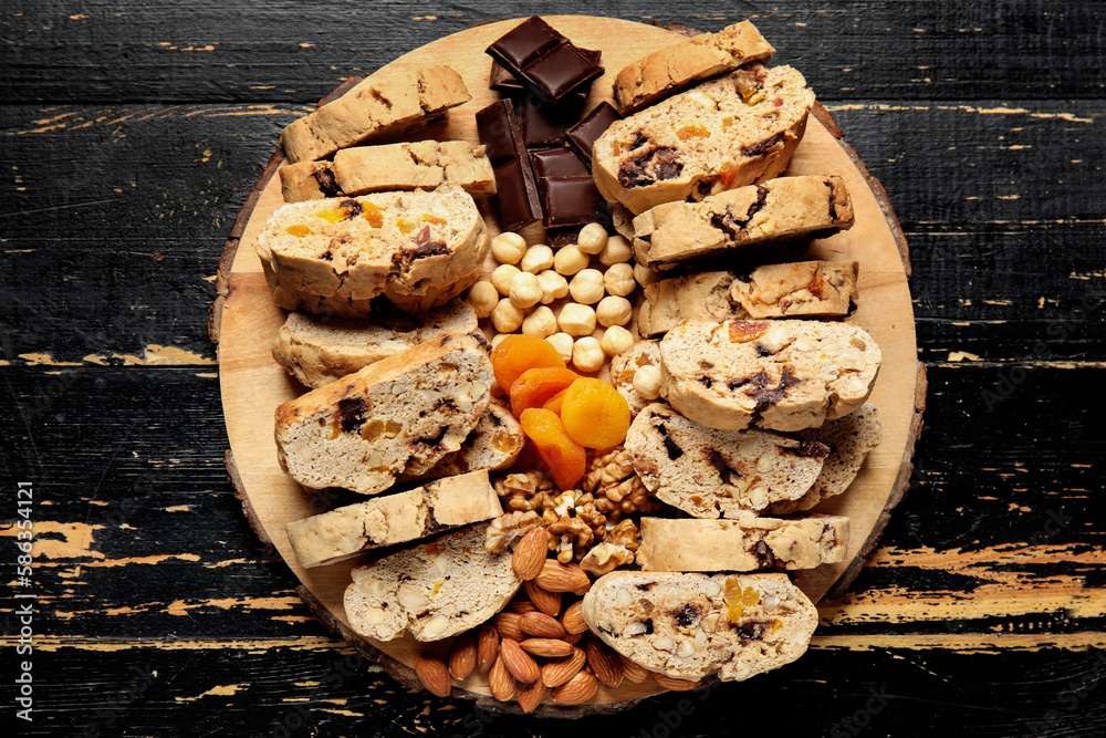 Board with biscotti cookies, nuts, dried apricots and chocolate on black wooden background