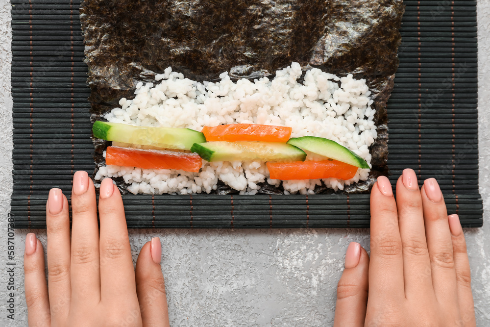 Woman preparing sushi rolls on light background