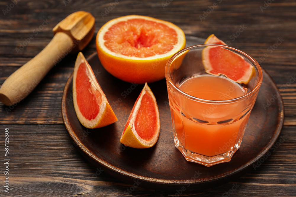 Plate with cut ripe grapefruit and glass of juice on wooden background, closeup