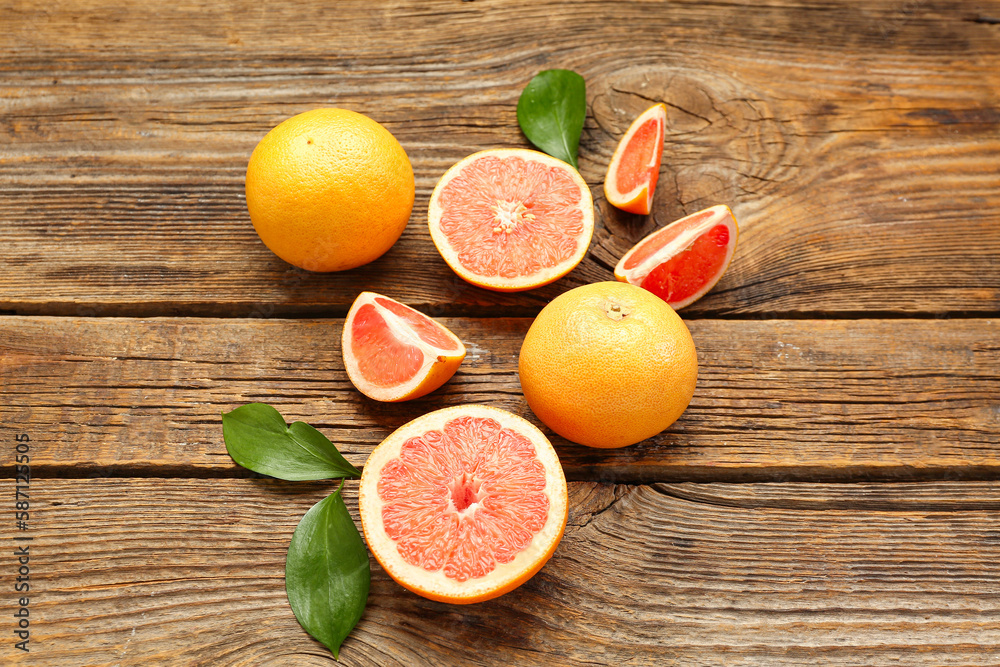 Composition with whole and cut grapefruits and plant leaves on wooden background