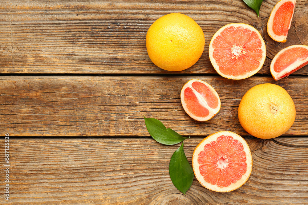 Composition with whole and cut grapefruits and plant leaves on wooden background