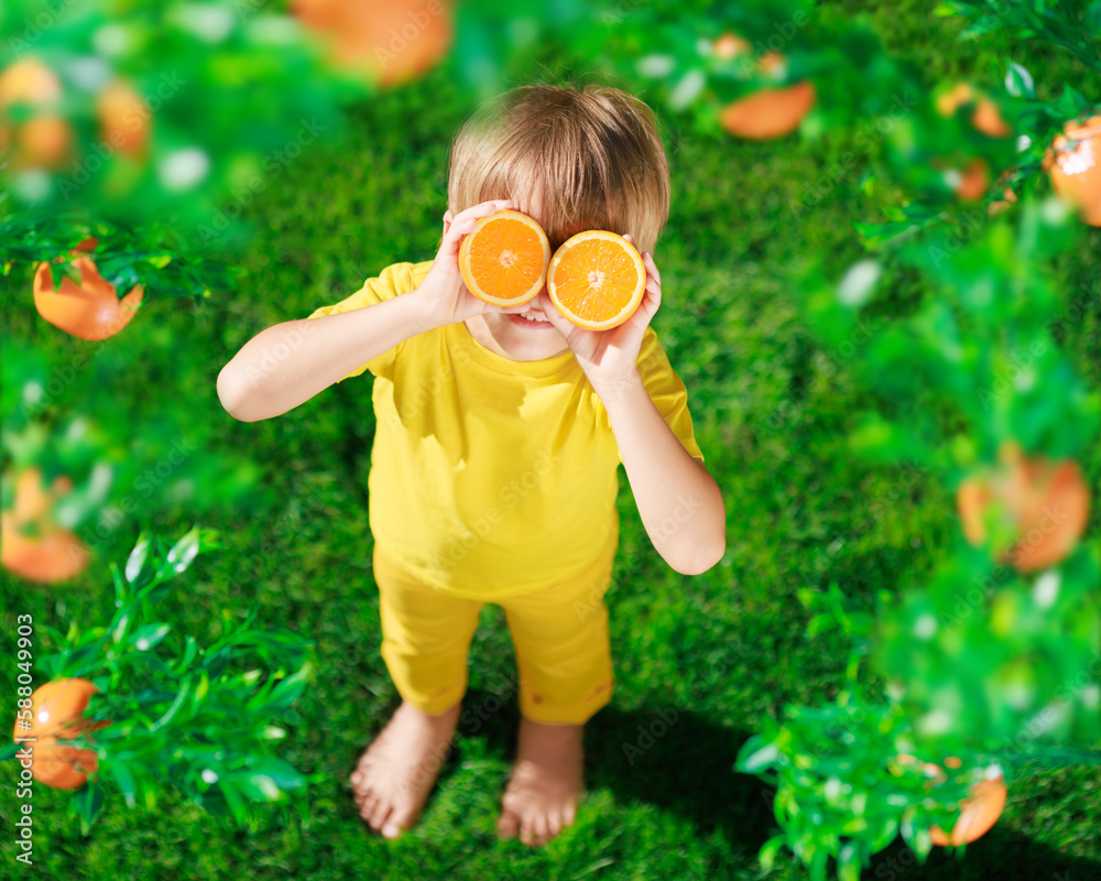 Surprized child holding slices of orange fruit like sunglasses