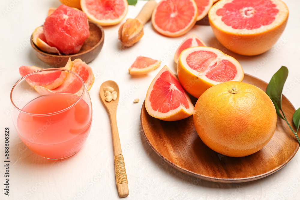 Wooden plate with ripe grapefruits and glass of juice on light background