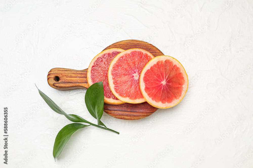 Wooden board with slices of ripe grapefruit and plant branch on light background
