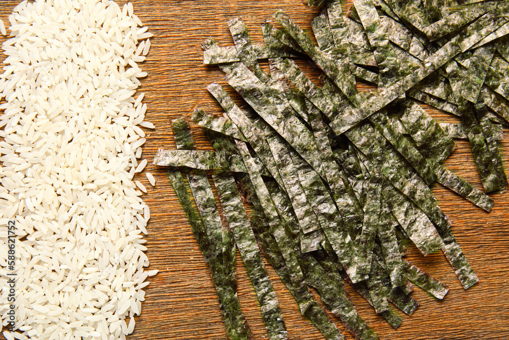 Wooden board with rice and cut nori sheets, closeup
