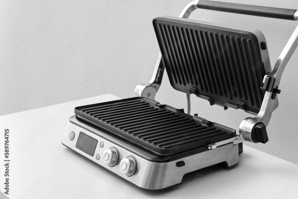 Modern electric grill with open lid on white table against grey background