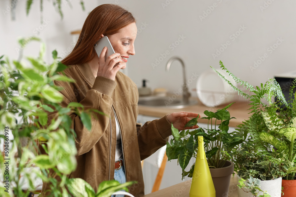 Young woman with green houseplants talking by mobile phone at home