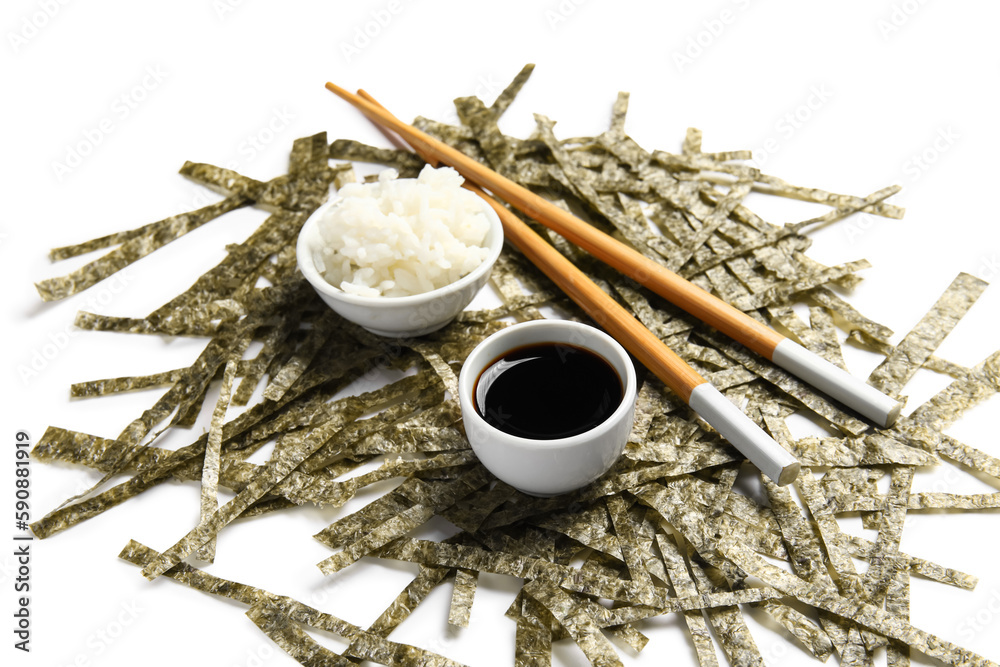 Heap of cut nori sheets, rice, soy sauce and chopsticks on white background