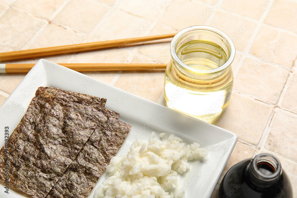 Plate with boiled rice, nori sheets, vinegar and soy sauce on light tile background, closeup