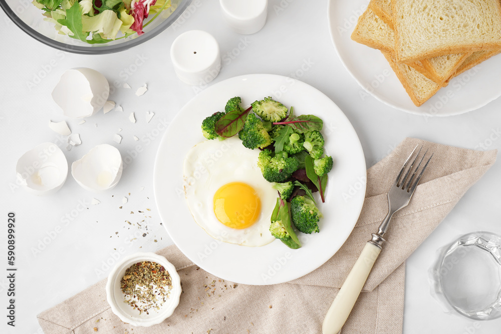 Plate with tasty fried egg, broccoli and spinach on light background