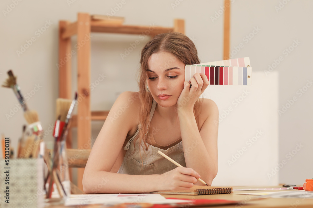 Female artist with paint color palettes writing in notebook at table