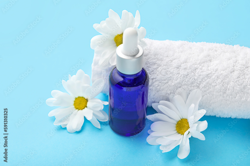 Bottle of cuticle oil, towel and chamomile flowers on color background