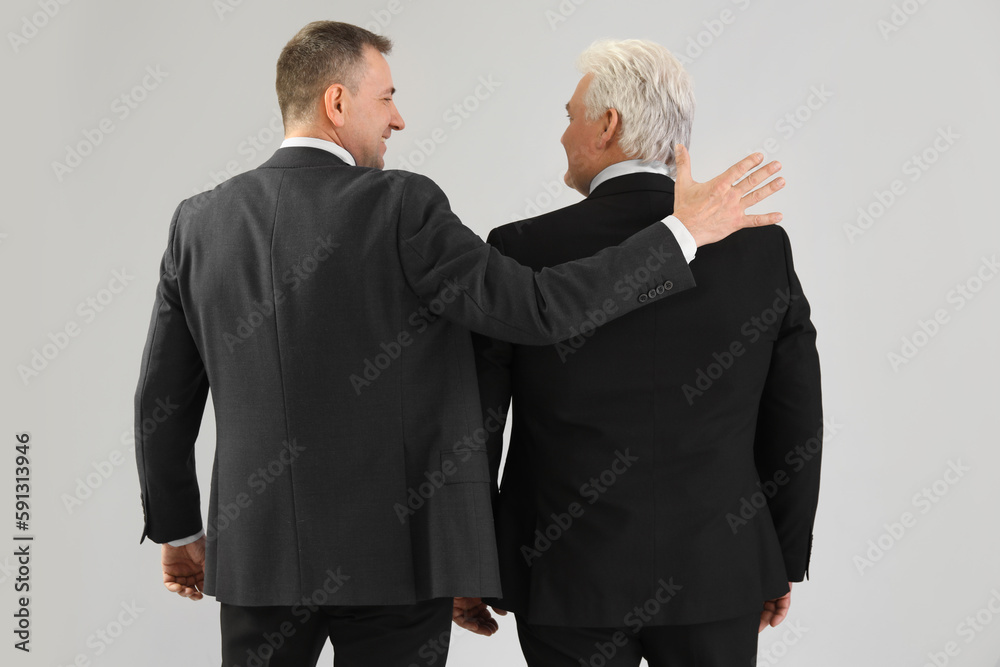 Mature brothers in suits on grey background, back view