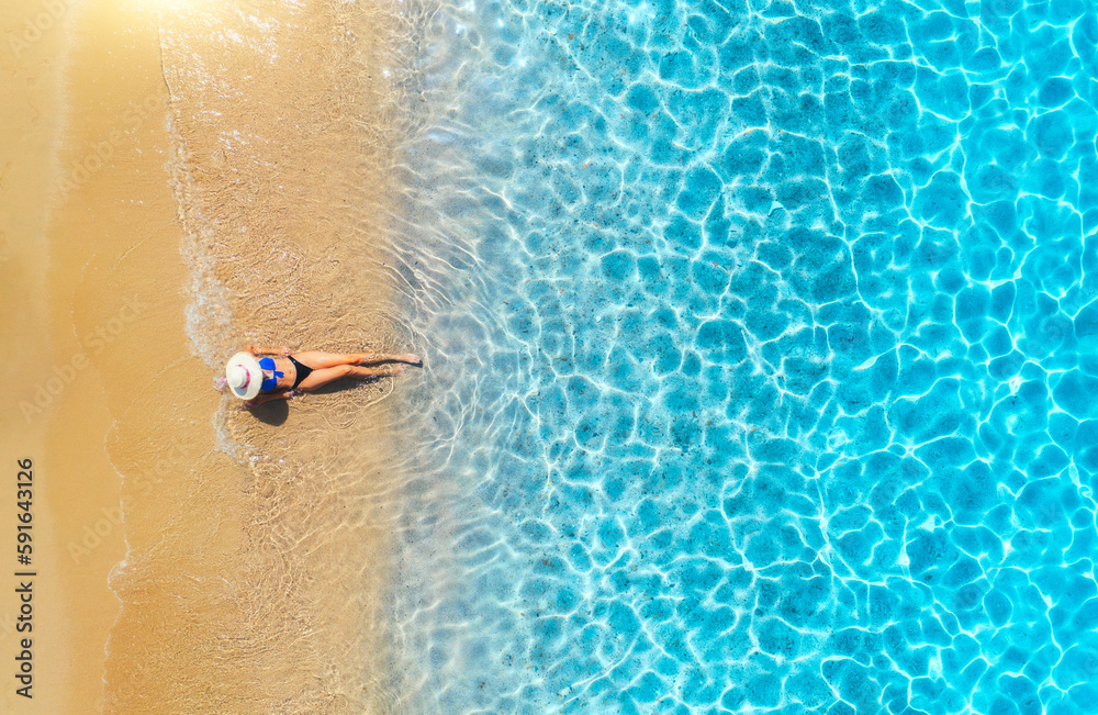 Aerial view of a lying woman in white hat on sandy beach and blue sea at sunset in summer. Tropical 