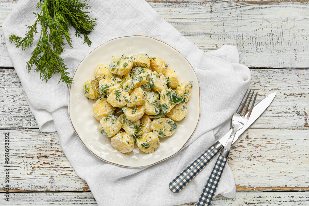 Plate of tasty Potato Salad with greens on light wooden background