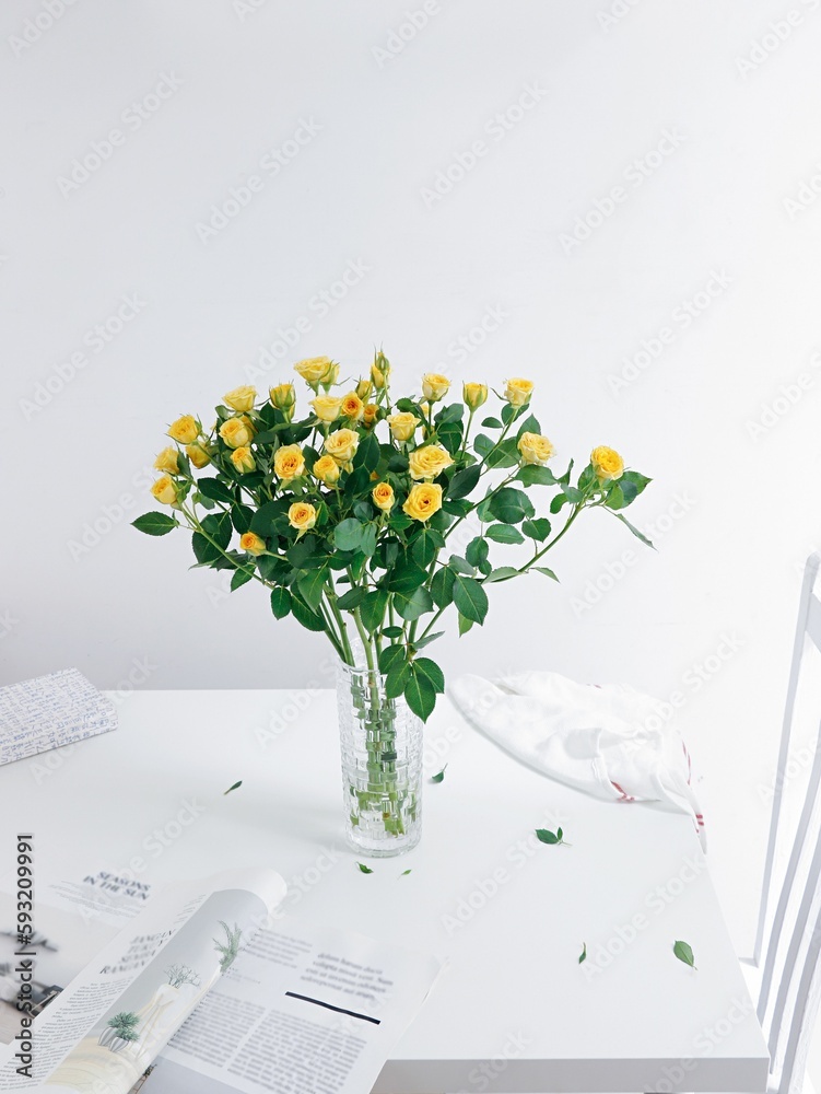 Vertical shot of a beautiful bouquet of roses in a glass vase on a white table with a magazine