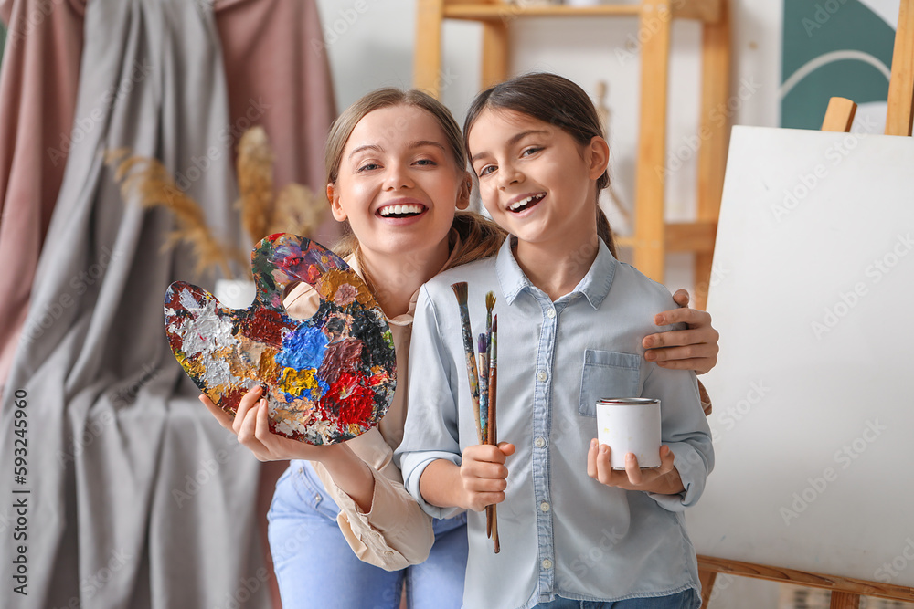 Little girl with paint brushes and her drawing teacher in workshop