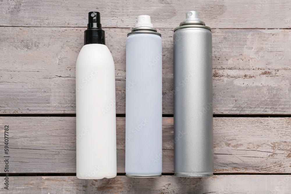 Different bottles of hair sprays on light wooden background