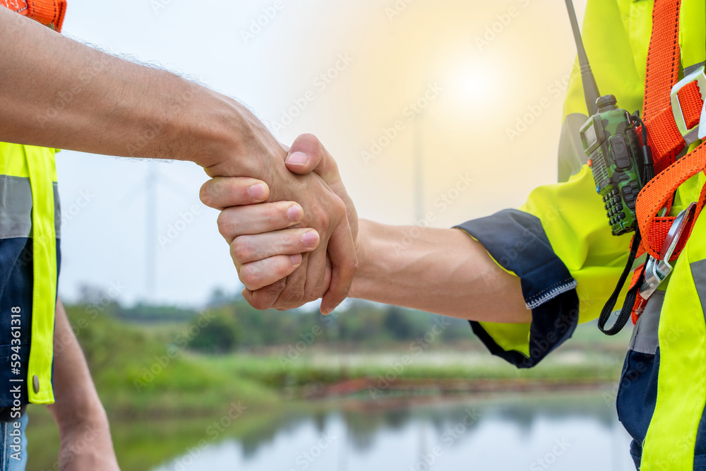 Engineers handshake after inspection work in wind turbine power generator station.
