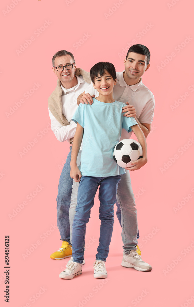 Happy little boy with his dad and grandfather holding soccer ball on pink background