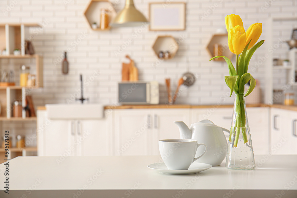 Cup, teapot and vase with beautiful tulip flowers on table in interior of modern kitchen
