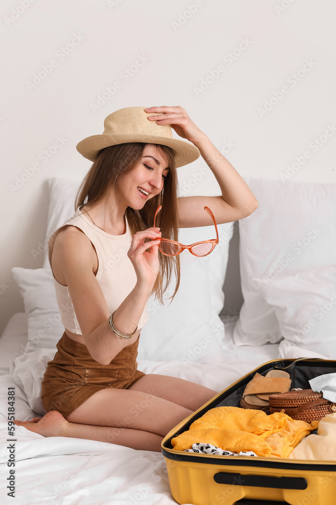 Young woman unpacking her beach accessories from suitcase in bedroom