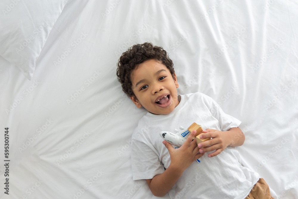 asian little boy sleeps on a soft bed, holding a toy with a big smile