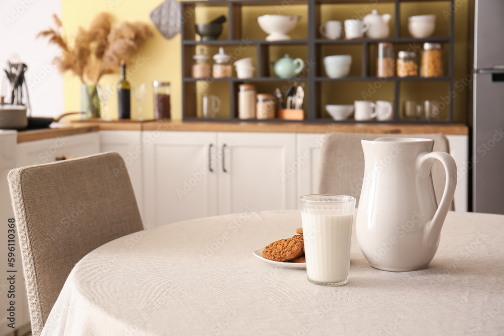Jug, glass of milk and plate with cookies on dining table in kitchen